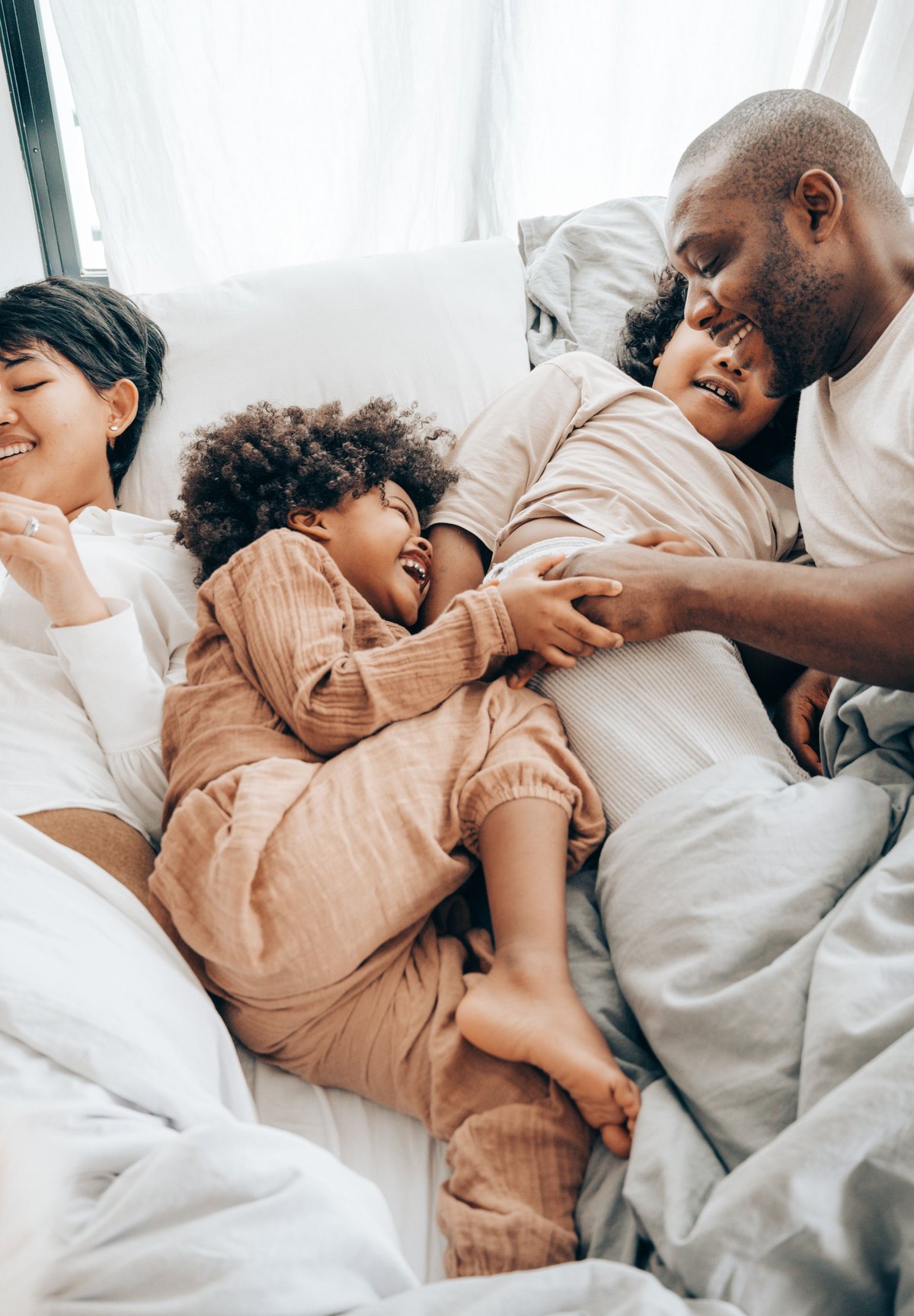Família deitada na cama sorrindo e brincando junta